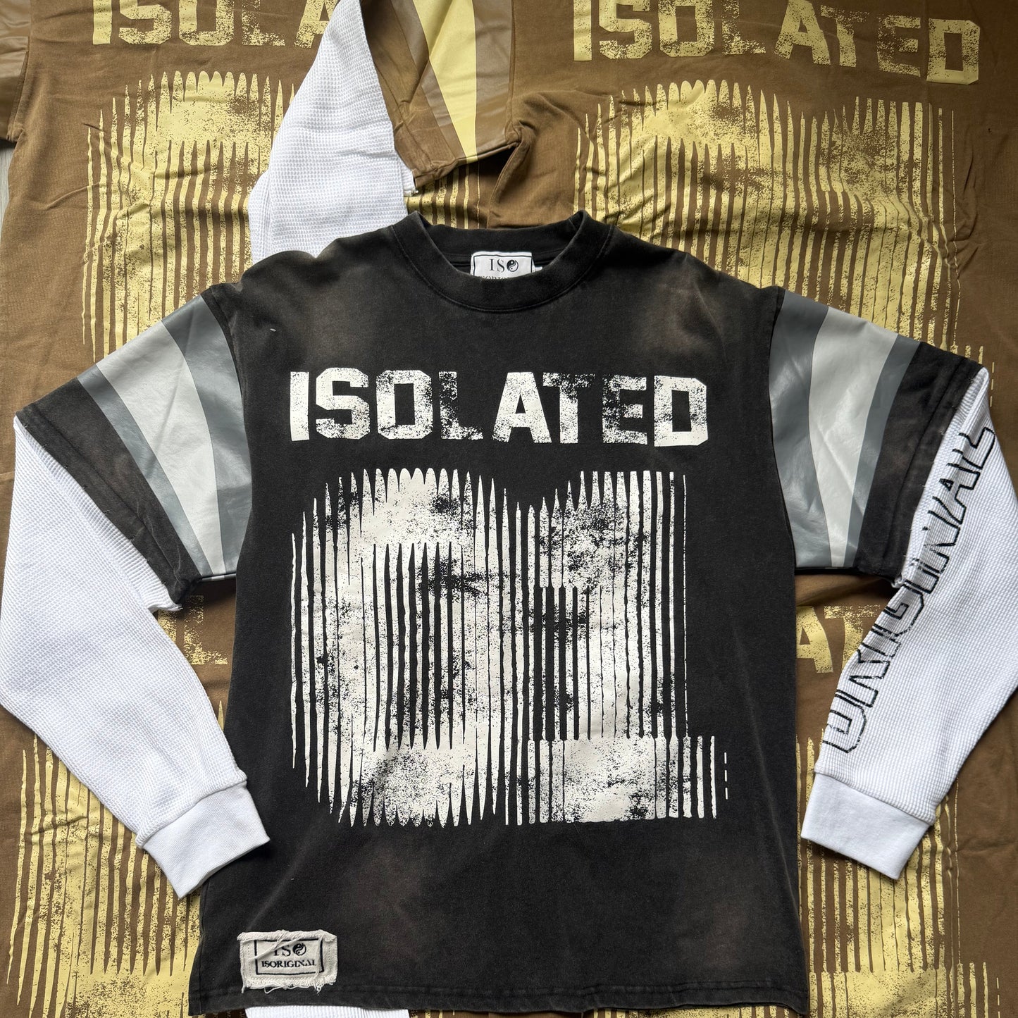 A black and white long-sleeve motocross jersey laid flat on a brown and gold patterned fabric backdrop. The jersey features a large distressed white graphic on the front with 'ISO.